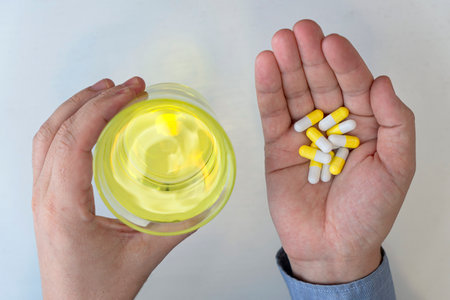 top view of man hand holding pills and glass of water on a white backgroundの写真素材