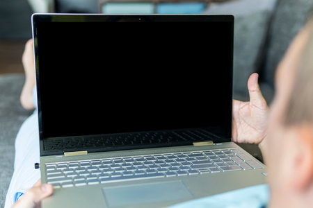 The man is lying on the sofa and looking at the empty black laptop screen. copyspace. The space is empty for text and designの写真素材