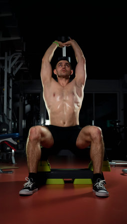 bodybuilder doing heavy weight exercise for biceps with dumbbell. the concept of sports and training. Muscular man with dumbbells in a dark gymの写真素材