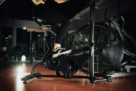 Closeup of spinning wheel on exercise bike on spin bicycle fitness workout. Woman training on stationary bike watching online video class for exercising cardioの写真素材