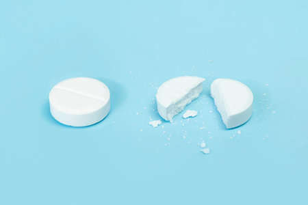 Two pills on a blue background, medicine, one tablet is broken in half. round tablet was divided...