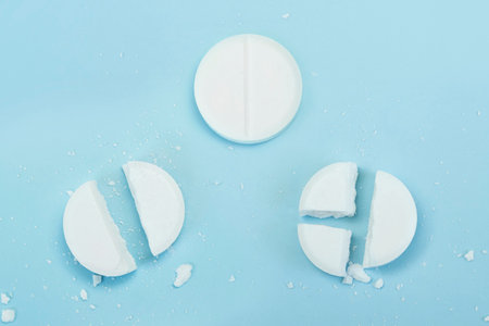 White pills on blue background. Few pills broken in half, reducing the dose of the medicine. round tablet was divided equallyの写真素材