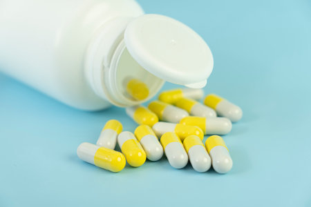 A pile of yellow pills scattered from a white plastic jar on a blue table. the concept of health medicine and pharmacy. production of medicines.の写真素材