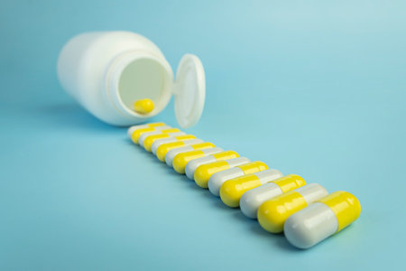 A pile of yellow pills scattered from a white plastic jar on a blue table. the concept of health medicine and pharmacy. production of medicines.の写真素材