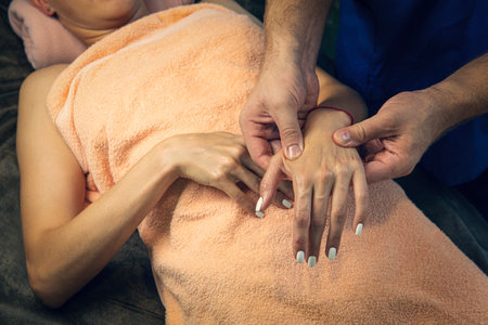 Beautician massaging hand of female spa salon client. A professional male masseur kneads the hand of a young woman.の写真素材