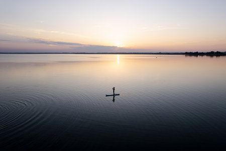 Girl paddling on SUP board on beautiful lake during sunset or sunrise, standing up paddle boarding...