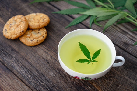 Cannabis tea herbal on tea cup and cookies with seeds with cannabis leaf marijuana leaves herb, health tea with hemp leaf plant THC CBD herbs food and medical - top view on a black table backgroundの写真素材