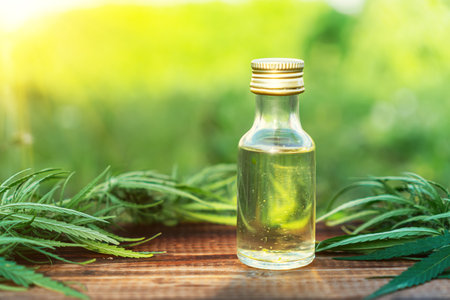 CBD oil hemp products. cannabis oil in a glass bottle and marijuana leaves on a wooden table on a green background of nature in daylightの写真素材