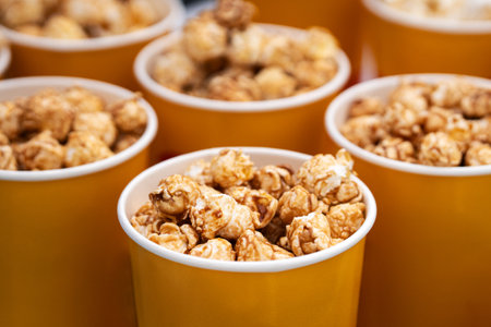 Paper bucket with popcorn, concept of watching TV or cinema. delicious sweet caramel brown popcorn. in a yellow orange glass close-up. boxes of popcorn on sale on the counter in the store.の写真素材
