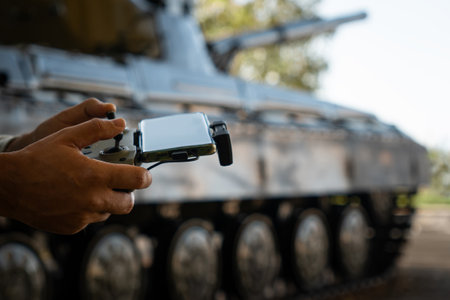 a man with a UAV control panel in his hands, a drone flying above the tank in the background in nature. help of reconnaissance drones in modern warfare.の写真素材