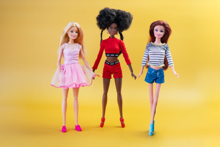 October 9, 2023. Barnaul, Russia: three dolls blonde, African-American and red-haired dolls on a yellow background. Barbie and her friends.のeditorial素材