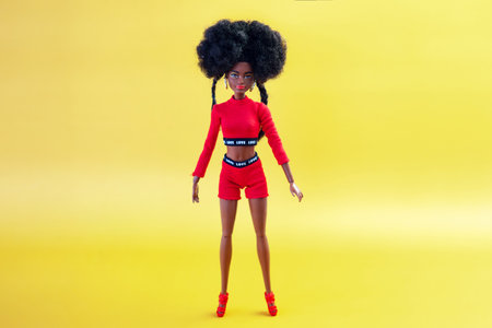 October 9, 2023. Barnaul, Russia: african american Barbie doll with black hair in a red suit standing on a yellow background.のeditorial素材