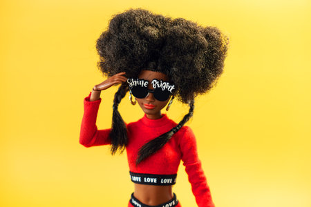 October 9, 2023. Barnaul, Russia: african american Barbie doll with black hair in a red suit standing on a yellow background.のeditorial素材