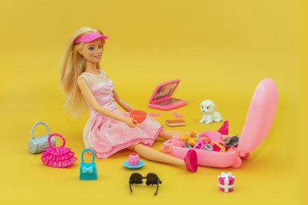 October 9, 2023. Barnaul, Russia: barbie is a traveler doll in a pink dress on pink background. doll is packing a suitcase. various accessories for playing with a doll.のeditorial素材