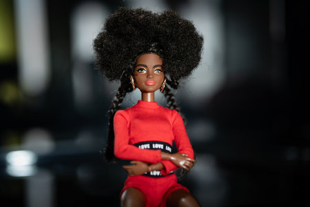 October 9, 2023. Barnaul, Russia: african american Barbie doll with black hair in a red suit standing on a dark background.のeditorial素材