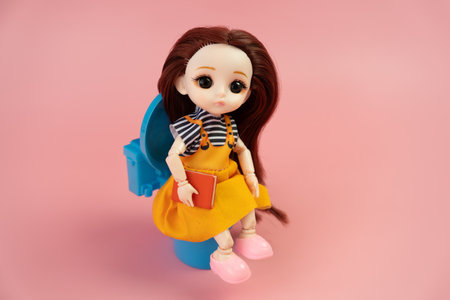 A drawing doll that uses a book in the toilet. a toy girl is sitting on the toilet on a pink background.の写真素材