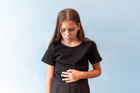 Young girl with bellyache on a blue background. A teenage girl holds her stomach with her hand.の写真素材