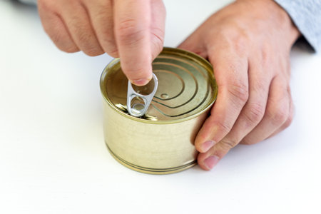opening a tin can on a white background. Hand holds canned food on white, man hands. an empty label for design and text. Copy Spaceの写真素材