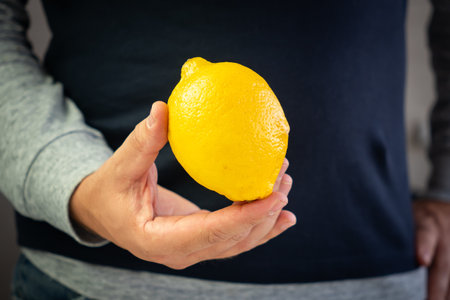 A male hand holds a yellow lemon. a man eats a lemonの写真素材