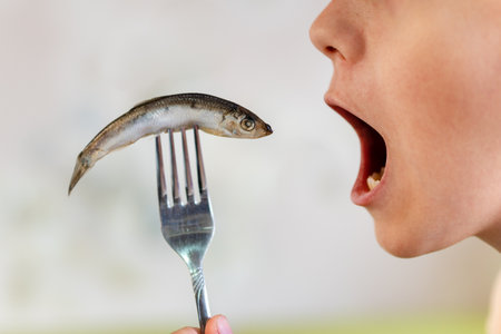 sprat in the hands, salty and fresh on a white background. the open mouth is eating fish.の写真素材
