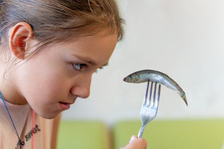 nasty fish. Children don't like to eat fish. A teenage girl looks with disdain at a sprat on a fork in her hand.の写真素材