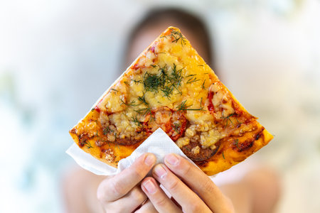 A young girl with plaits is eating a piece of pizza