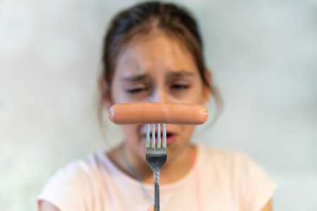 not Delicious fast junk food. Close-up. A teenage girl looks at a boiled sausage with dislike. Tasteless fast food.の写真素材