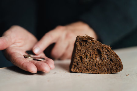 Hands of senior woman with bread and coins on wooden background. Poverty concept. A handout of bread for the poor. the concept of poverty and hunger.の写真素材