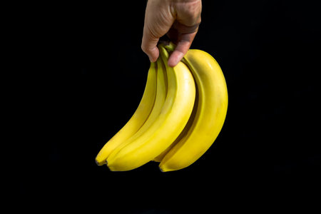Cropped view of hand with ripe yellow bananas, on black background.の写真素材