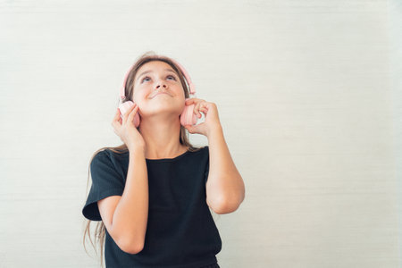 Happy smiling child girl with eyes closed enjoys listens to music in headphones. Vivid and fun emotions, happy child with pleasure listens to songs in wireless headphonesの写真素材