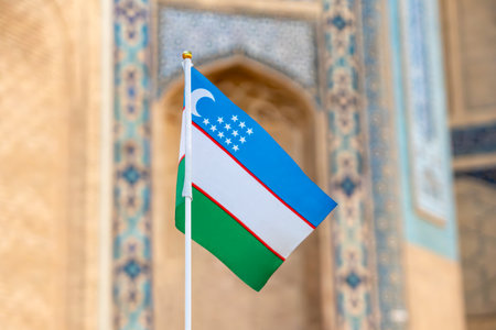 Waving Flag of Uzbekistan against the background of the madrasah. Uzbekistan a small souvenir flag symbol of the state on wavy cotton fabric.の写真素材