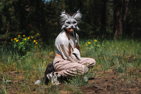 A girl in a cat mask on the background of a green park. People are animals. Sports quadrobics