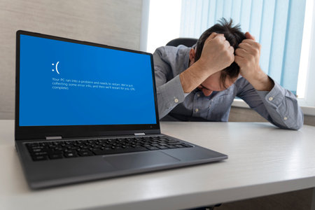 showing error blue screen on the Laptop against the background of an angry upset man clutching his headの写真素材