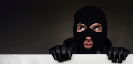 An evil thief in a mask looks out from behind a white board. Space for text and design. copy space....