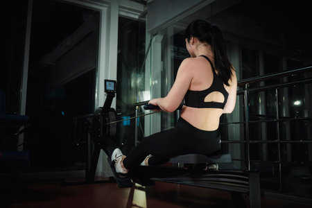 Purposeful fit brunette in sportswear sitting on simulation rowing exercise machine. Functional...