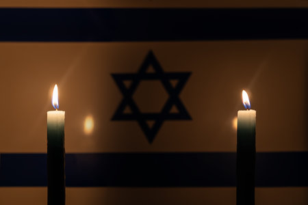 Mourning in country Israel. A burning candle on the background of the Israeli flag. Victims of cataclysm or war concept. Holocaust Memorial Day, remembrance day. National mourning. war in Middle Eastの写真素材
