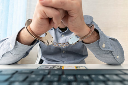 a man in handcuffs is sitting at his workplace with a computer and money in dollars.. The concept of bribery and criminal crimes in the cyber sphere. internet censorshipの写真素材