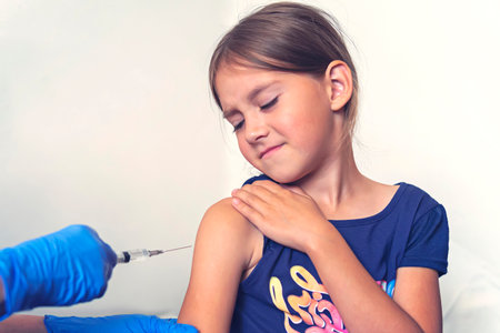 The girl is vaccinated in her hands on a white background in the hospital. Routine vaccination against flu and colds. Prevention of the spread of coronavirus infection.の写真素材