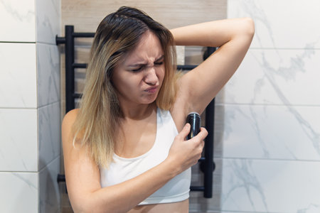 A young woman lubricates her armpits with a roll-on antiperspirant close-up. The smell of sweat from the armpits is a concept.の写真素材