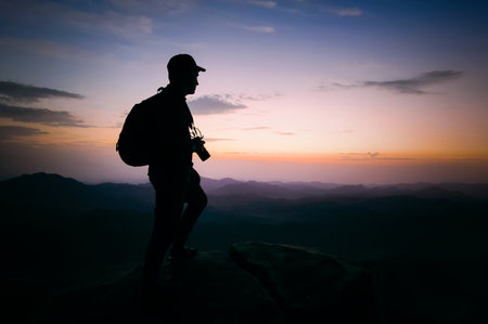 Photographer silhouette outdoor on hill with copy space for use. A tourist on top of a mountain with a camera and a backpackの写真素材