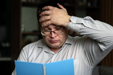 A man holds a blue notebook in his hands, making notes with a pencil. He prepares the curriculum at home.の写真素材