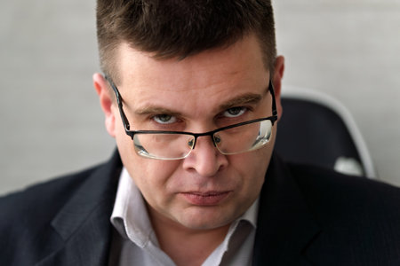 Stern Middle Age Man in Suit looking over Spectacles. A businessman man in glasses with a serious look looks piercingly at the camera.の写真素材