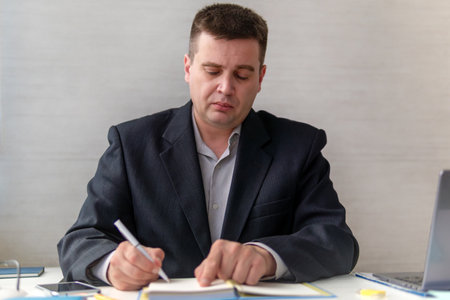 A man holds a notebook in his hands, making notes with a pen. He is preparing the curriculum at...