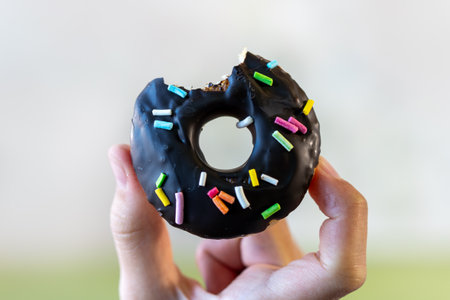 a piece of a chocolate donut in the hand of a teenage girl was bitten off.の写真素材