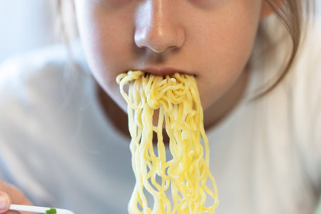 Cute asian child girl eating delicious instant noodles with fork.の写真素材