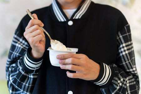 Hands holding yogurt pack, girl eating yoghurt. Light meal, snack. Milk product. Diet. Cream dessert.の写真素材
