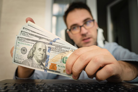 Man sitting at desk with money on PC keyboard background, wages, bonus concept. US dollars in male...