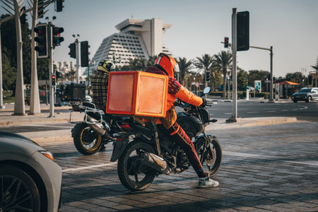 A food delivery courier is driving an order to a customer's home on a moped. takeaway food during quarantine. transport delivery of parcels at home. motorcycle rider with big backpackの写真素材