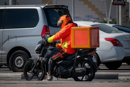 A food delivery courier is driving an order to a customer's home on a moped. takeaway food during quarantine. transport delivery of parcels at home. motorcycle rider with big backpackの写真素材