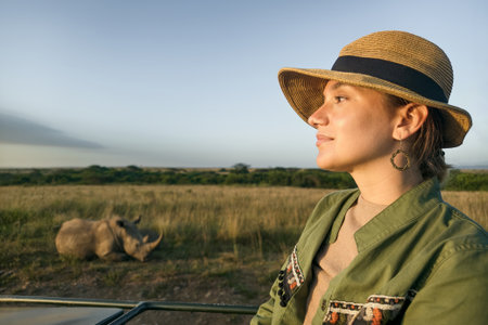 Young woman discover african nature by car with an open roof Tanzania safari. A Caucasian girl in a hat looks at animals in the savannah. The concept of travel and adventure in the wild.の写真素材